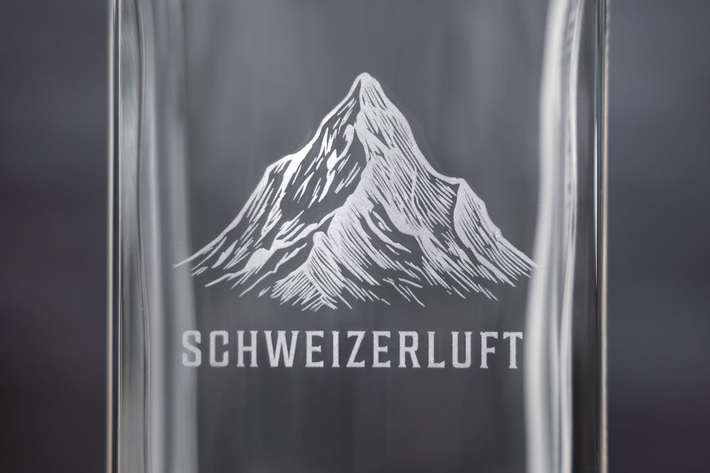 Close-up of engraved Swiss mountain and SchweizerLuft® logo on glass bottle.